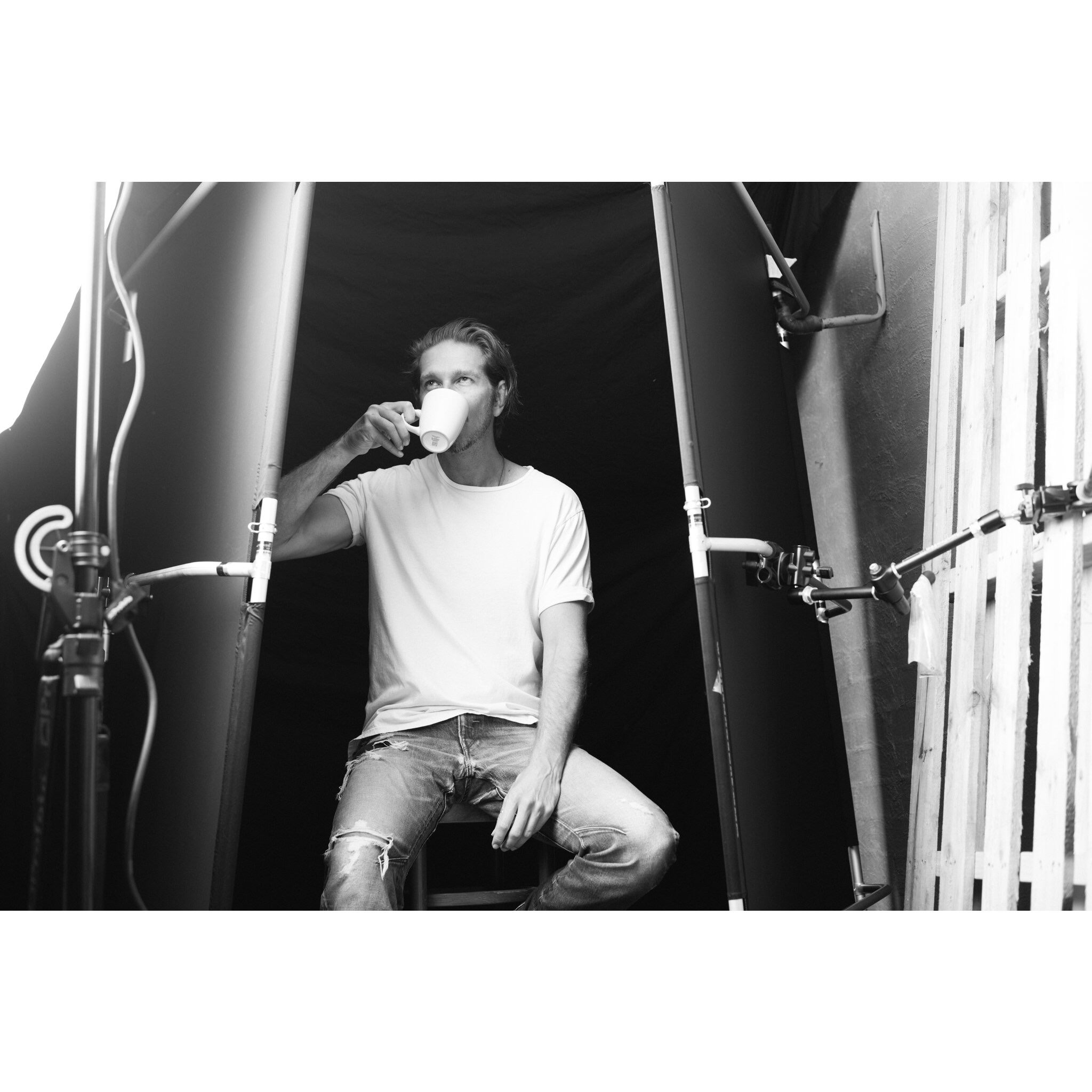 Black-and-white photograph of Dave Blake taking a tea break beside studio backdrops and lighting stands