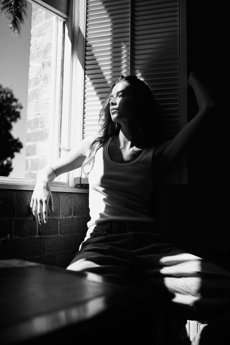 Jess Holiday seated in bands of hard light and shadow beside a louvred window