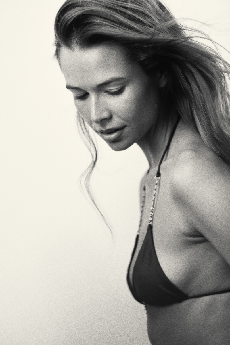 Warm-toned portrait of Jess Holiday looking down in black swimwear