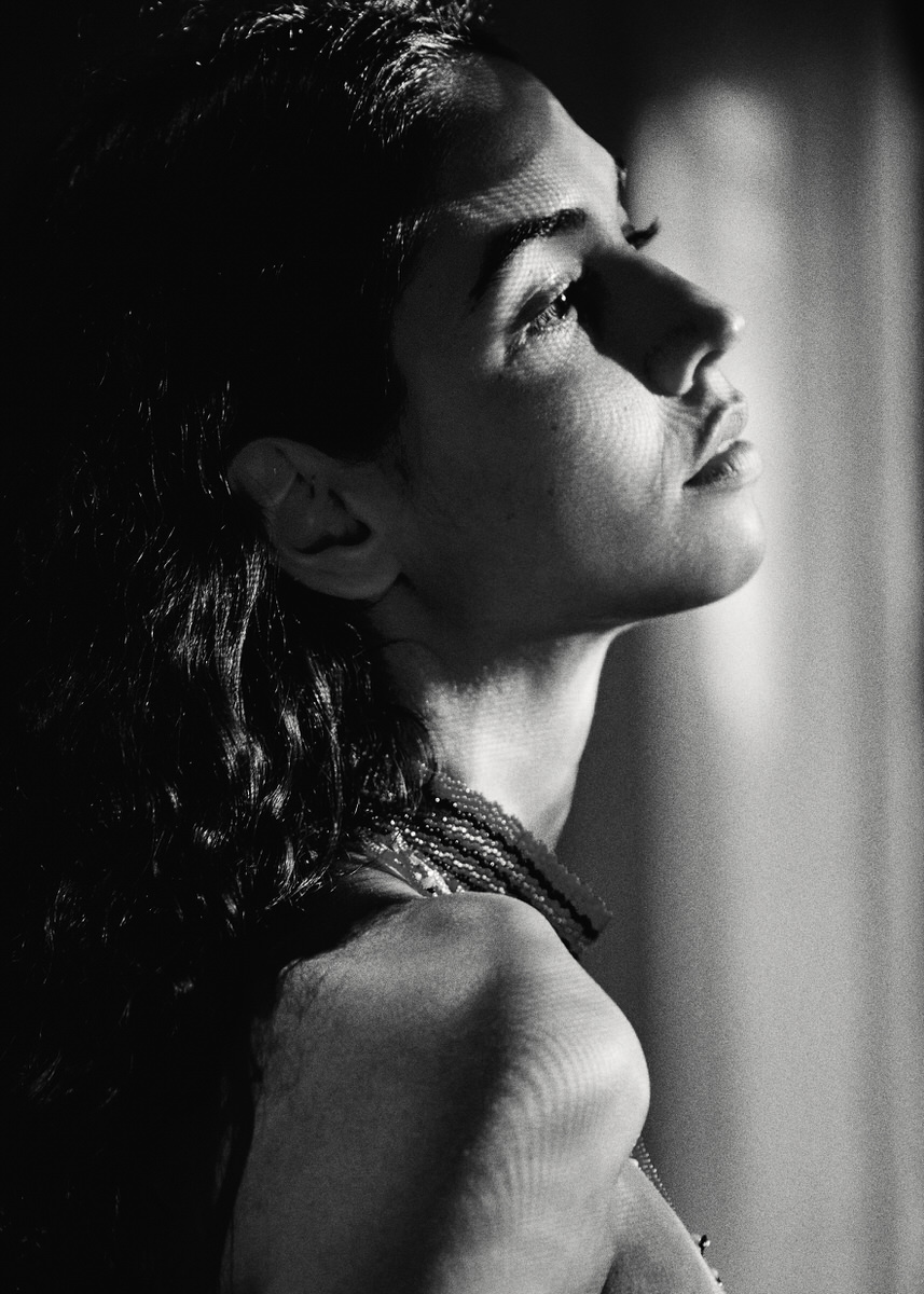 A close black-and-white profile portrait of Naomi looking upward in patterned window light