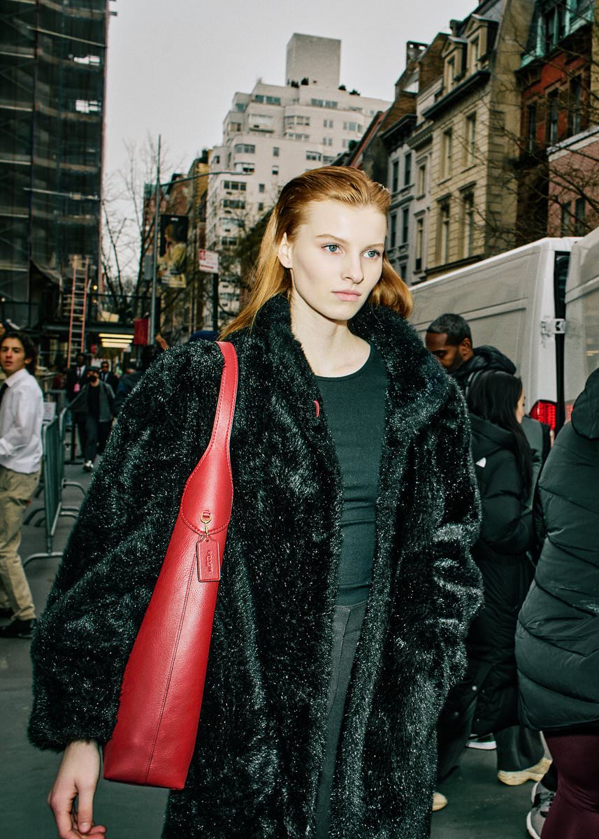 Lainey Hearn in a black coat carrying a red Coach shoulder bag on a New York street