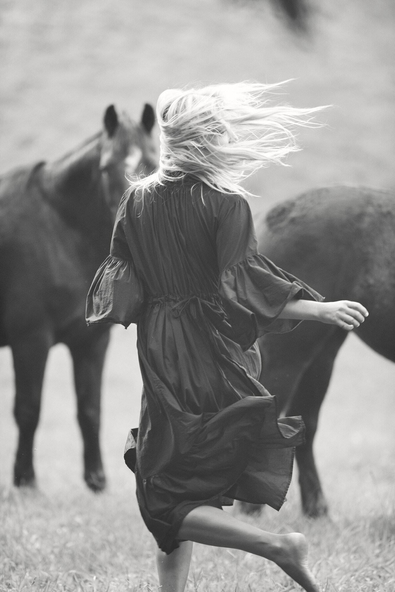Black-and-white photograph of a flowing dress and windswept hair beside a horse