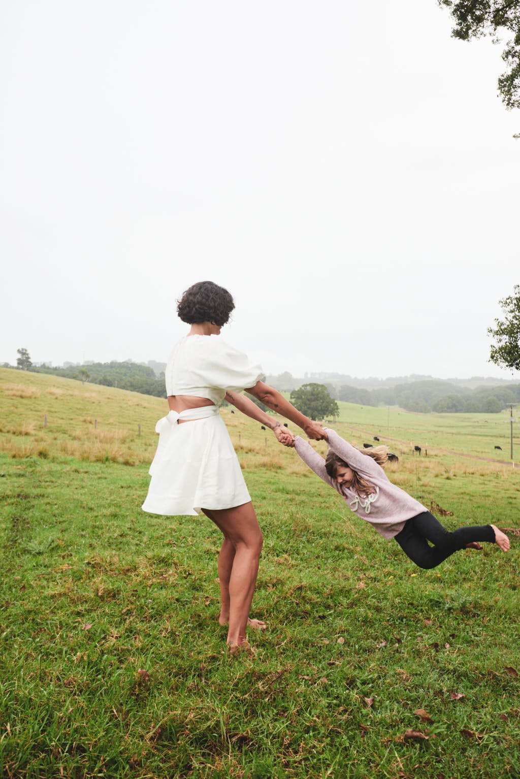 Steph Carta in a white Aje dress, swinging a child in a field