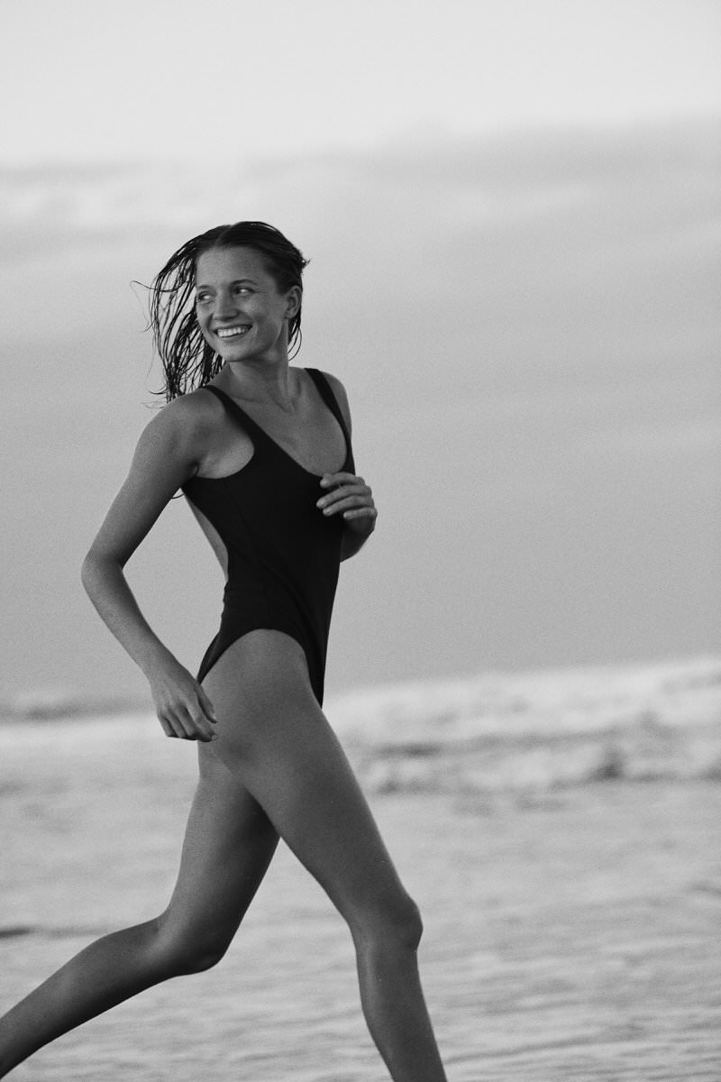 Black-and-white photograph of Camilla Muller walking at the water’s edge